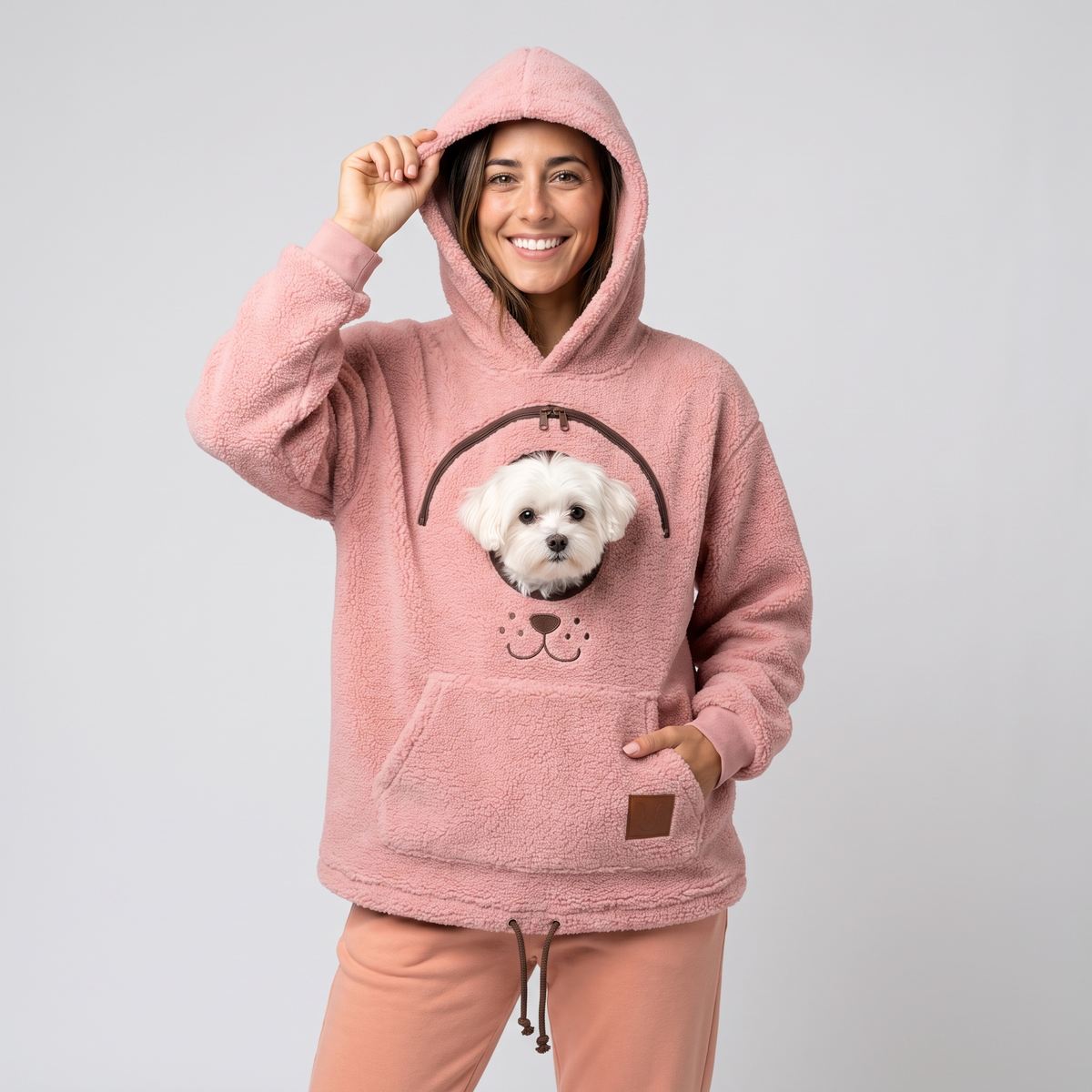 Woman wearing the pink CozyPaws pet pocket hoodie with a white Maltese peeking out of the chest window