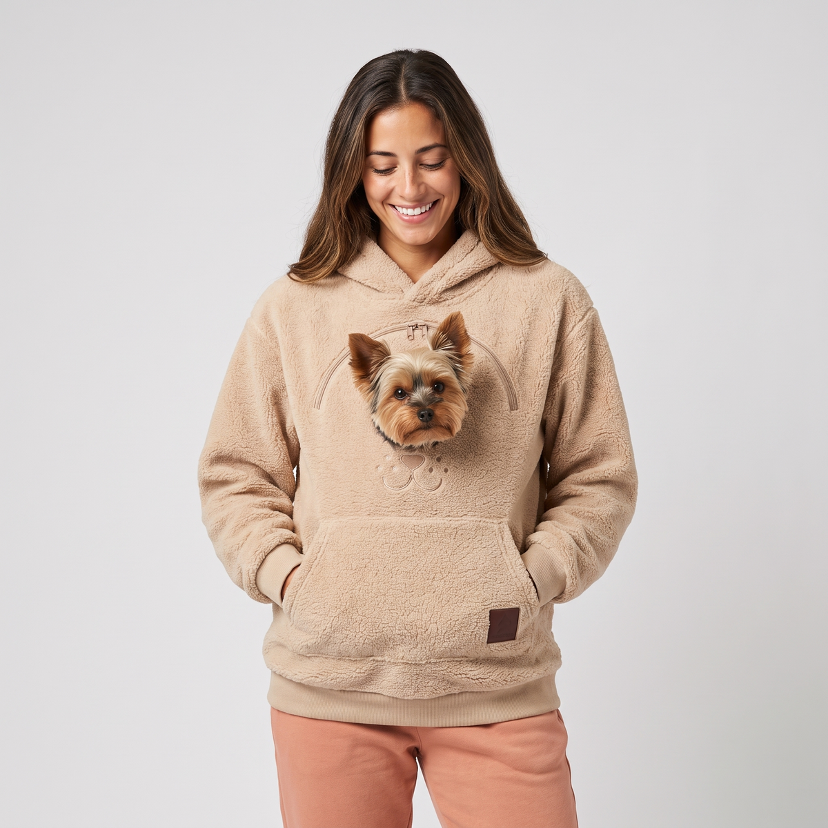 Woman wearing the beige CozyPaws pet pocket hoodie with a Yorkshire Terrier peeking out of the chest window