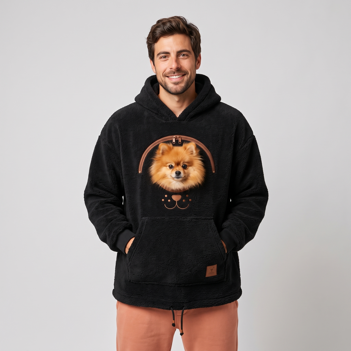 Man wearing the black CozyPaws pet pocket hoodie with a Pomeranian peeking out of the chest window