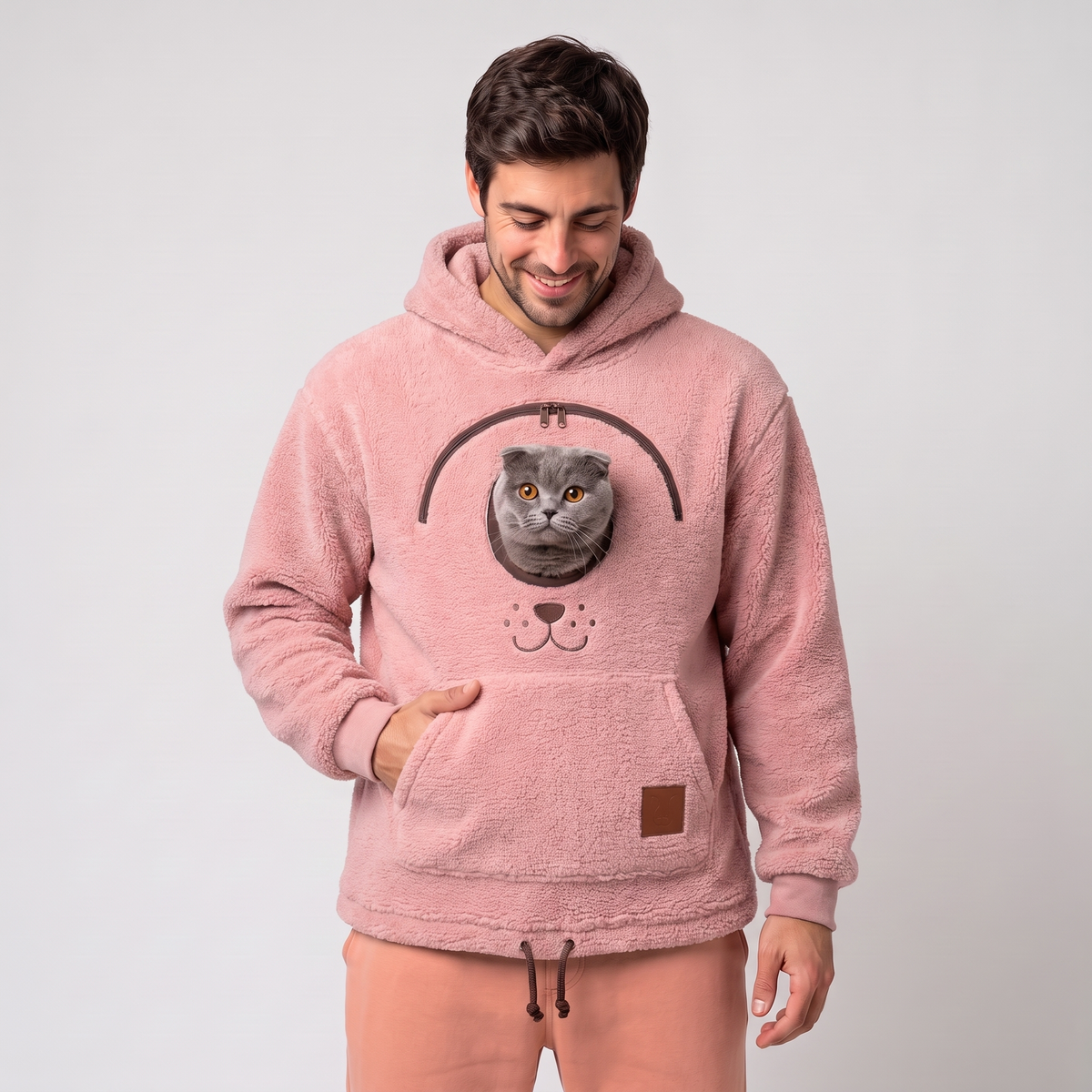 Man wearing the pink CozyPaws pet pocket hoodie with a Scottish Fold cat peeking out of the chest window